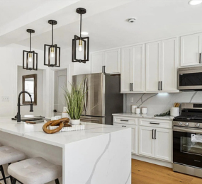 Expertly crafted modern kitchen remodel with a quartz waterfall island, custom shaker cabinets, stainless steel appliances, and bold black accents—showcasing quality craftsmanship and attention to detail.