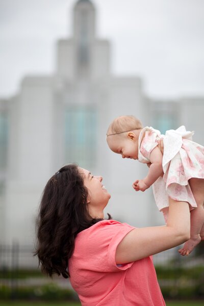 A mom holding her daughter above her, while they smile.