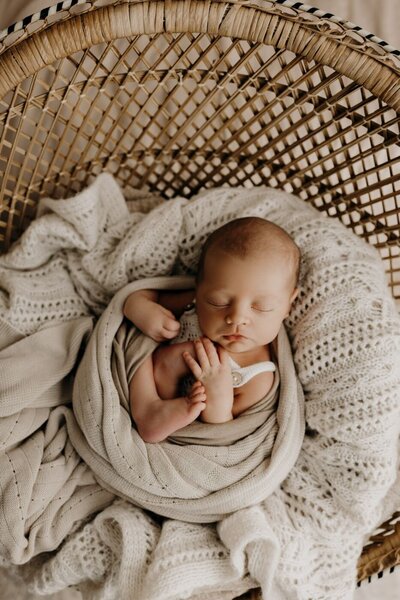 Peaceful newborn infant with closed eyes, wrapped in neutral tones, nestled in a basket, photographed in Mullingar, Ireland