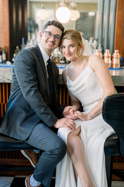 Newlyweds hold hands while seated at a stylish bar. Captured in elegance by Jackson Ms Wedding Photographer.