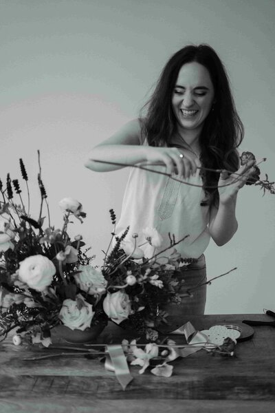 Vrouw die breed glimlachend een bloemstuk aan het maken is