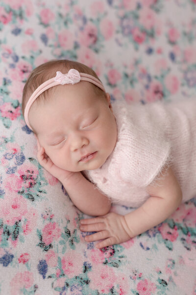 Newborn girl laying on a floral blanket with hand under her face