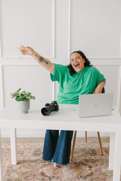 A person sitting on a desk holding a glass out with one hand