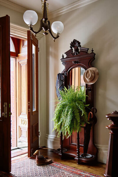Brownstone interior decorators in Boston designed a restored South End brownstone entry with original stair, vintage rug, antique hall tree, and historic light fixture.