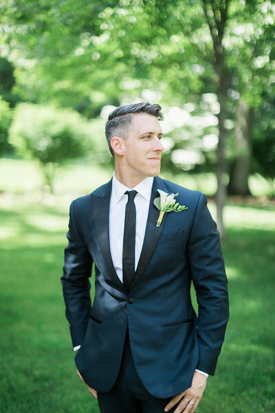 Groom smiling and looking away from camera surrounded by green trees