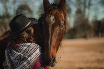 Girl in cowboy hat holds into the neck of a rescue horse during her elopement.