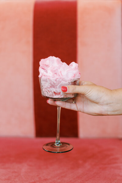 Hand holding coupe glass in front of a red couch