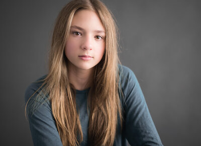 striking portrait of teen with long blonde hair in dark teal shirt against grey backdrop