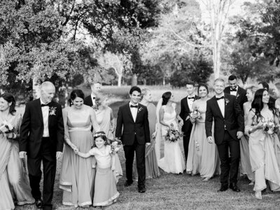 Black and white photo of bride and groom walking with family and wedding party