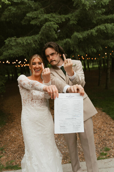 bride and groom holding up ring finger and marriage license