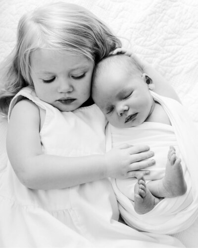 a sweet black and white image of an older sibling and newborn sleeping