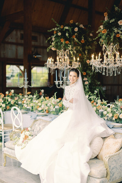 Bride in a long elegant dress sitting in front of a table decorated with lots of floral centerpieces