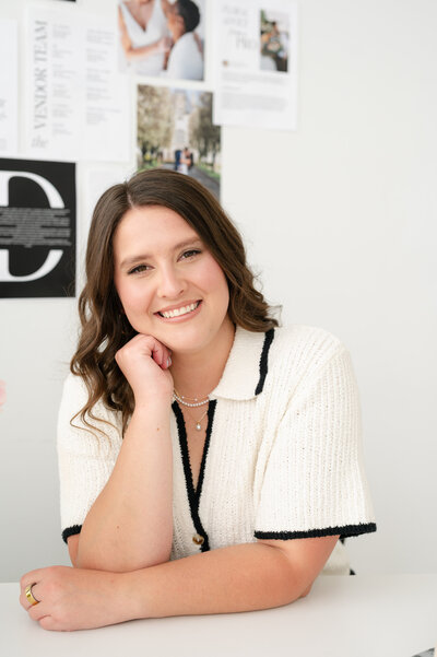 Wedding Photographers in Rhode Island | Kelsey Sheehan Photography Timeless Rhode Island Weddings | Kelsey smiling, leaning on a white desk with an old-fashioned phone. Tulips in a vase, and a collage of photos and quotes on the wall.