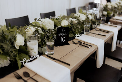 Black and white wedding table number with custom calligraphy at a farm table with lush florals