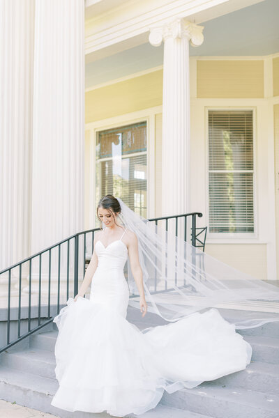 A bride walks down the steps while holding up her Vows Bridal dress.