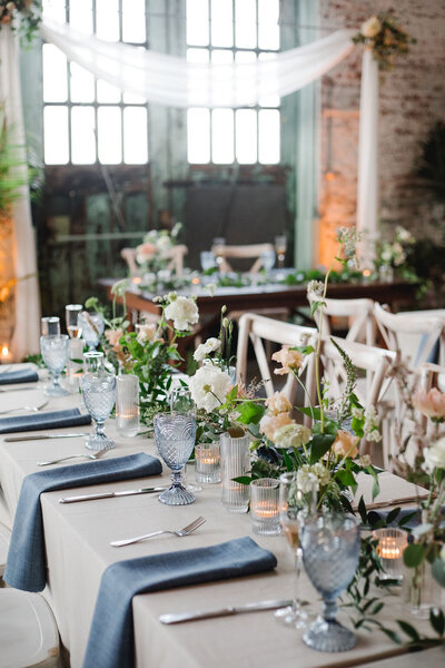 Close-up of wedding reception table with luxurious floral centerpiece of pink roses, eucalyptus, and white blooms by Leigh Florist