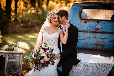 Wedding couples photo sitting on vintage truck kissing.