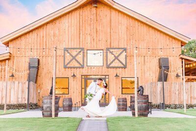 The groom dips his bride in front of the barn at Camelot Meadows.