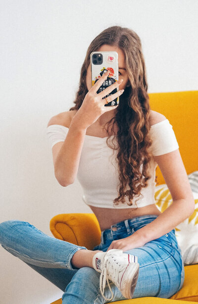 Woman taking a selfie for her Instagram feed sitting on a yellow couch