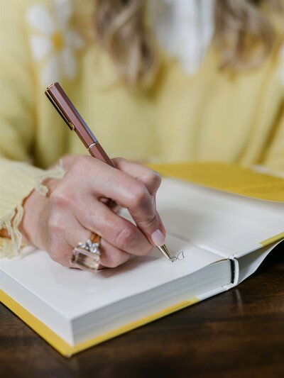 Phillipa Leseberg, a budding author, writes in a yellow notebook using her favorite pen. Her clothing complements the vibrant pages she fills with ideas.