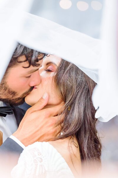 A couple kisses under a wedding veil.