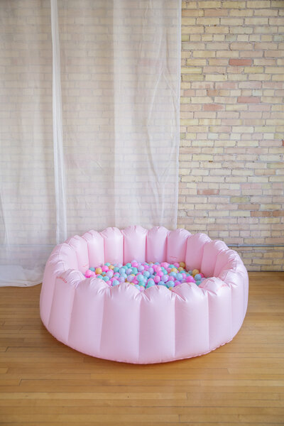 A pink scalloped ball pool with pastel balls inside.