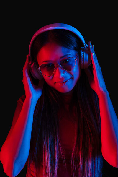 Neon photo of girl wearing large headphones and heart sunglasses, covered in blue and ambient red lighting