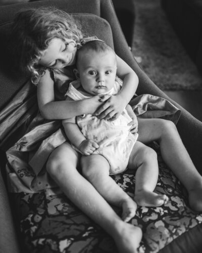 black and white image of curly haired toddler holding baby brother