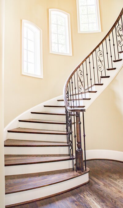 A large wooden spiral staircase  in a room with cream walls, wood floors and large rising windows.