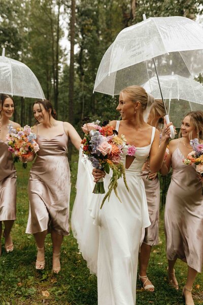 Bride and her bridesmaids sharing a moment under umbrellas on a rainy August day.