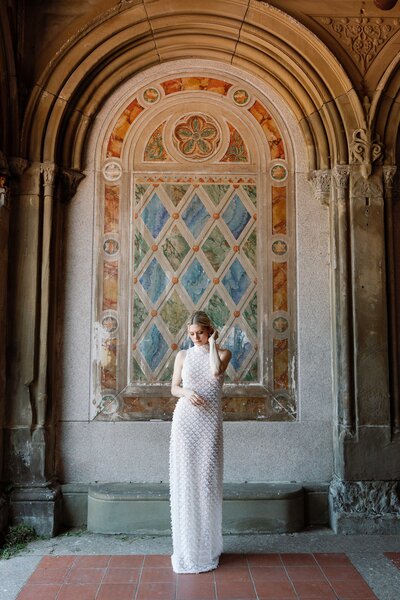 Bride stands in long gown in front of historic archway at Bethesda Terrace in Central Park.