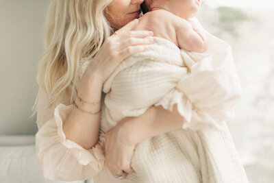 A tender close-up of a mother cradling her newborn baby wrapped in a soft cream blanket, emphasizing the connection and warmth of motherhood in their Kansas City home. 