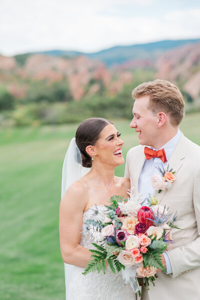 A couple kisses in the middle of a field with a large red rock formation behind them aptured by denver wedding photographer