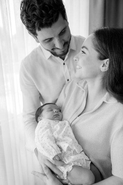 Een jong gezin, stralend en gelukkig, koestert hun pasgeboren baby in een lichte en serene setting.