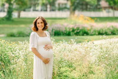 pregnant mother wearing a white dress in a park with white flowers in her Oak Park, IL maternity photos