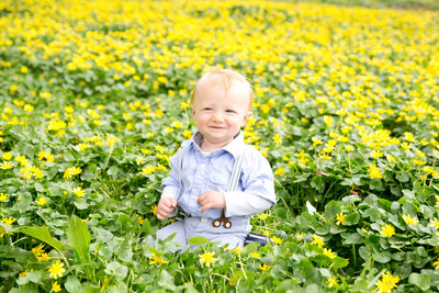 Baby boy sits in field of yellow flowers smiling at camera