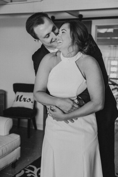 Black and white photo of groom holding bride from behind while bride laughs by Iowa City wedding photographer Sabrina Wilham