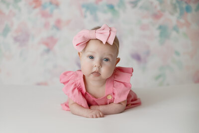 4 month old girl looking straight at the camera. in her pink outfit and bow
