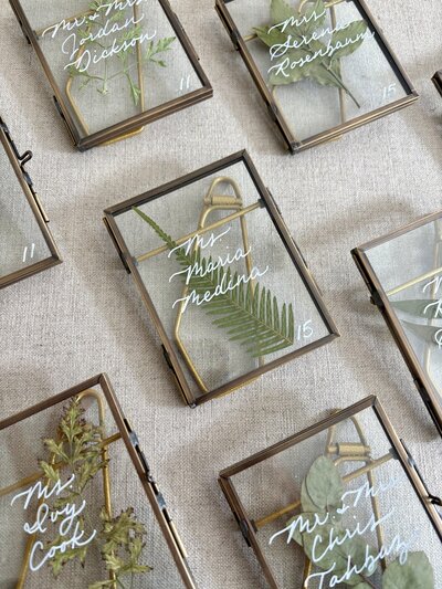 Glass frames with pressed florals and white handlettering escort cards for wedding at Kontokosta Winery in Northfork, New York.