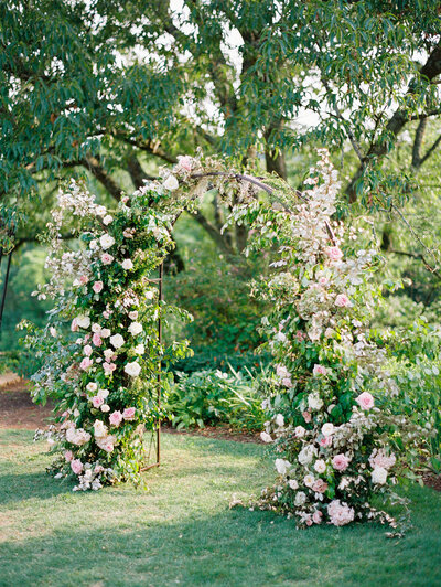 Spring floral arch in pinks, creams, white, sage for outdoor wedding. Roses and blooming branches highlight this wedding ceremony. Design by Rosemary and Finch in Nashville, TN.