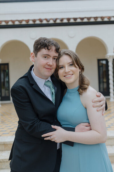 Zack and Shavonne smiling and hugging in a stylish outdoor setting, dressed in formal attire.