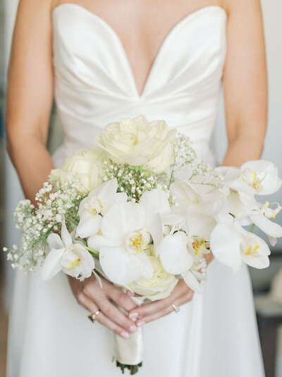 Bride in white dress holds bouquet of white flowers