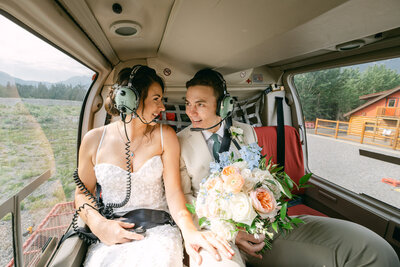 This joyful photograph captures the bride and groom laughing together inside a flying helicopter as they soar over Banff National Park, Alberta. The exhilarating experience and stunning aerial views add to the excitement and adventure of their special day, creating a moment full of happiness and connection.
