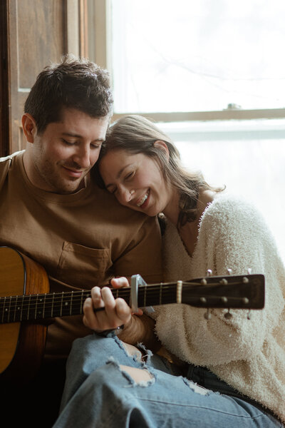 man holding guitar and sitting next to woman on couch