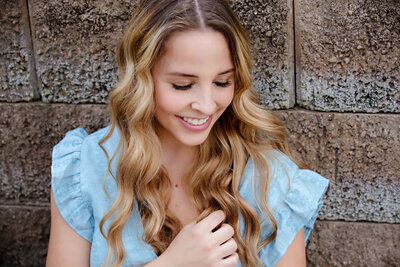 Sweet HS Senior portrait taken in Charlotte NC. Young lady has a blue dress, blonde hair and is looking down with a sweet giggly smile.
