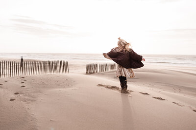 Fotoshoot meisje rent over strand met zee en paaltjes op achtergrond jas wappert open