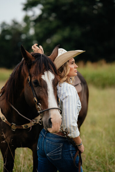 woman wearing a cowgirl hat while looking off in the distance beside her horse