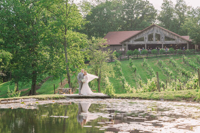 A couple at The Vineyard at High Holly at sunset in June overlooking a pond enjoying their destination wedding photos