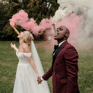Séance couple dans un château en région parisienne, ce couple mixte s’amuse avec des fumigènes colorés le jour de leur mariage – une scène joyeuse et moderne captée par un duo photographe vidéaste