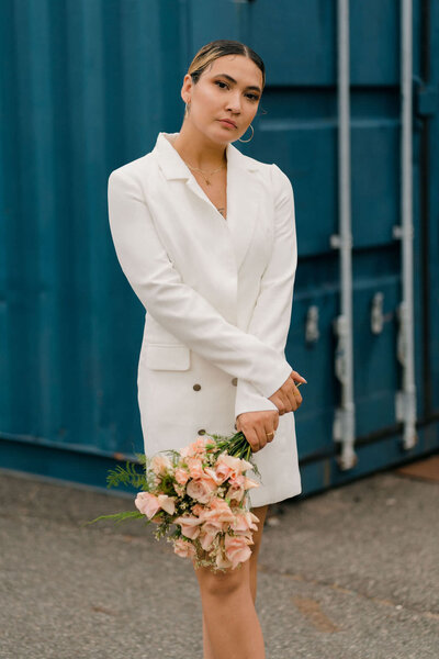 bride standing in front of a shipping container holding her bouquet down by her knees